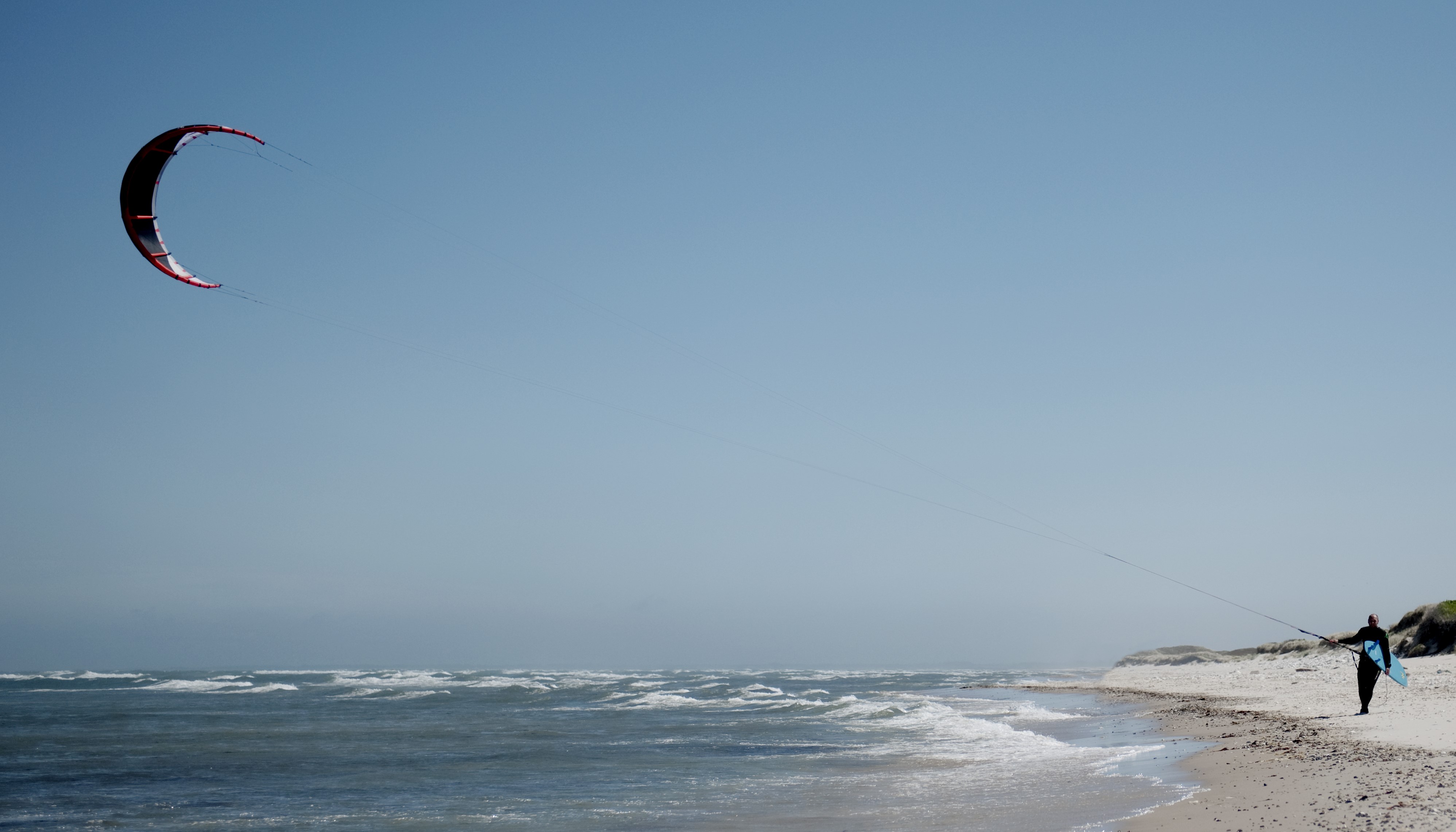 Hav, kitesurfer går på stranden med sin kite.jpg