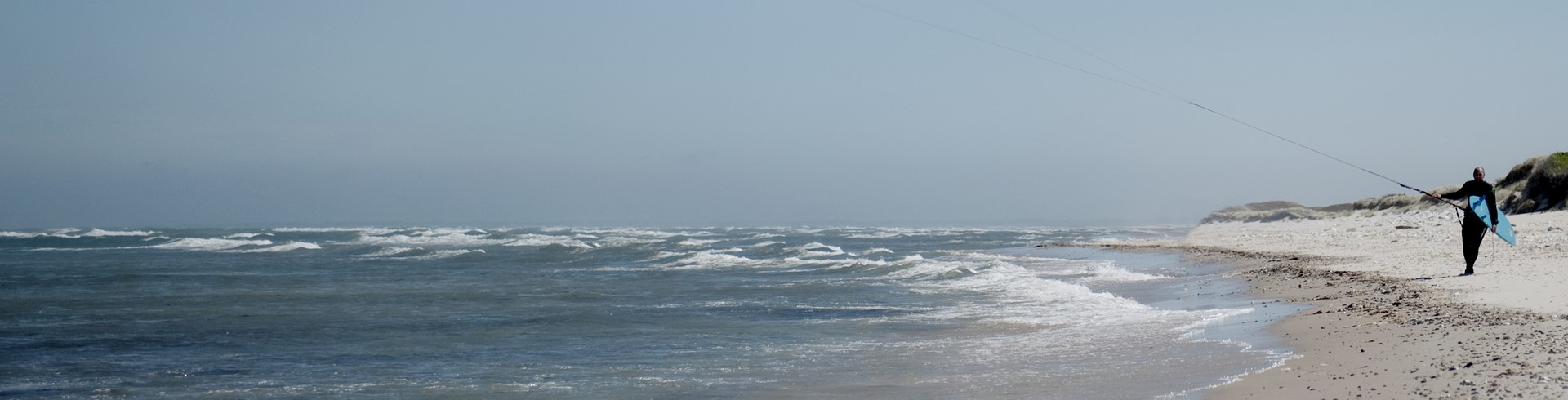 Hav, kitesurfer går på stranden med sin kite.jpg